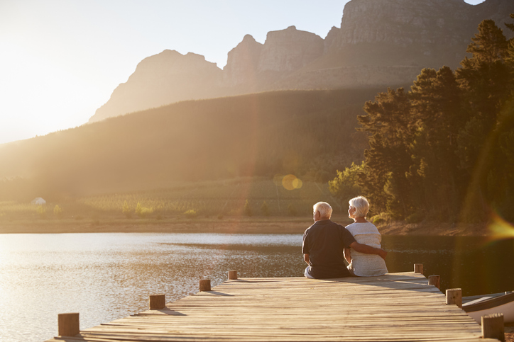 Senior Couple Sitting On Wooden Jetty By Lake