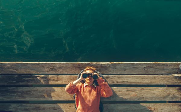 Girl Lies On A Pier Near The Sea And Looks Through Binoculars On Tje Sky