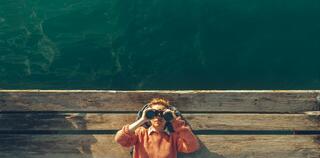 Girl Lies On A Pier Near The Sea And Looks Through Binoculars On Tje Sky