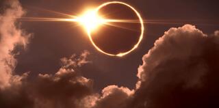 The moon covers the sun in a solar eclipse with a few clouds
