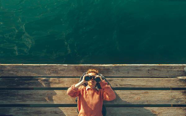 Girl Lies On A Pier Near The Sea And Looks Through Binoculars On Tje Sky