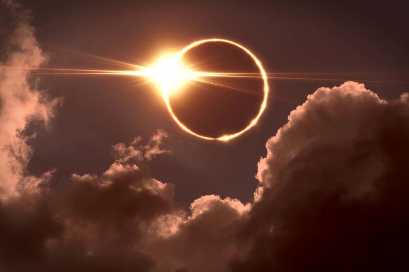 The moon covers the sun in a solar eclipse with a few clouds